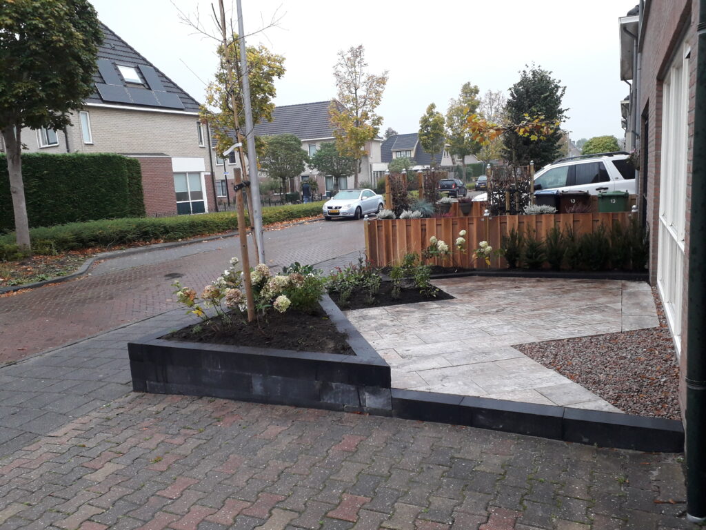 Moderne tuinaanleg met verhoogde plantenbak, klinkerbestrating en decoratieve beplanting in woonwijk