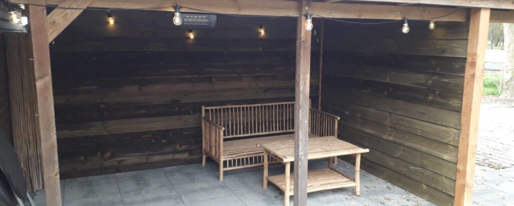 Houten tuinhuis met overkapping en tuinmeubilair, voorzien van sfeerverlichting voor gezellige buitenmomenten