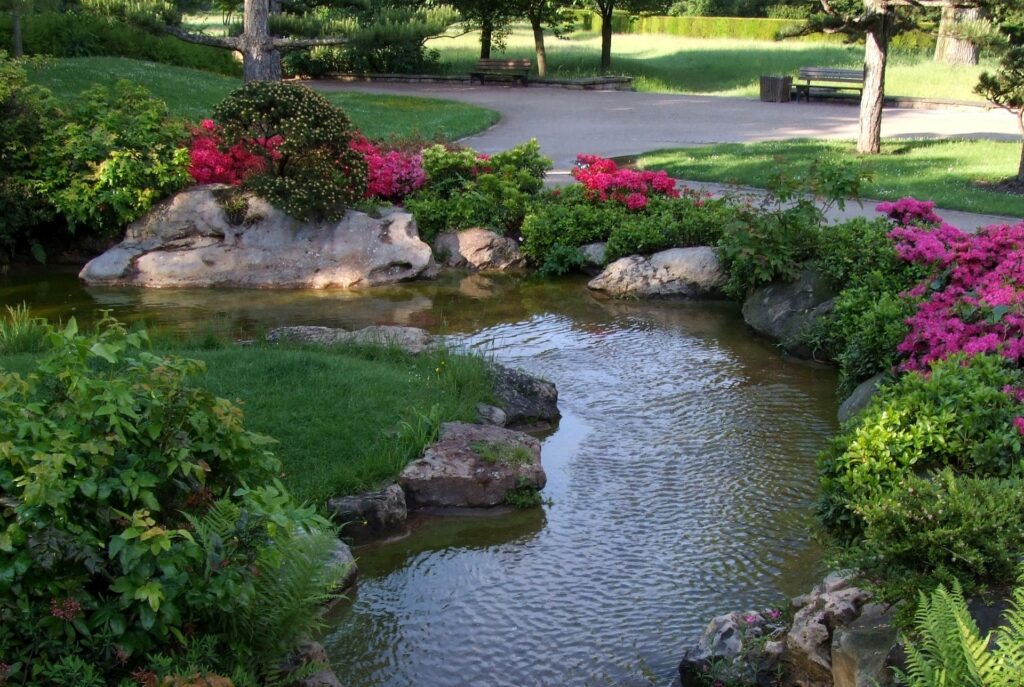 Aangelegde vijver met waterpartij, natuursteen en kleurrijke bloemen in professioneel ontworpen tuin